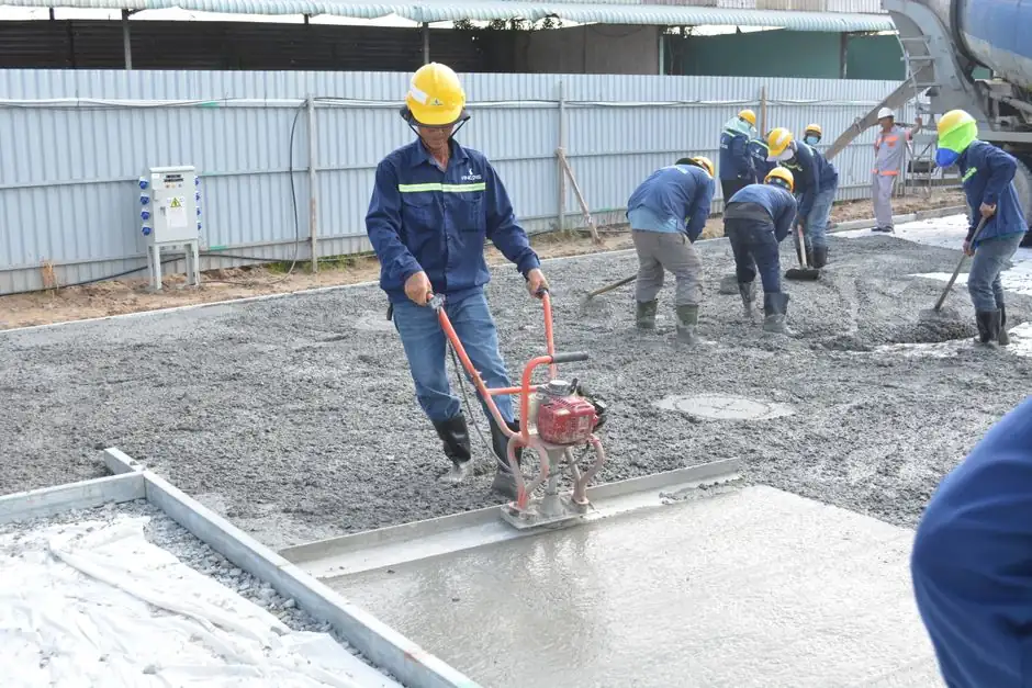 Team of workers smoothing and leveling wet concrete at a construction site.
